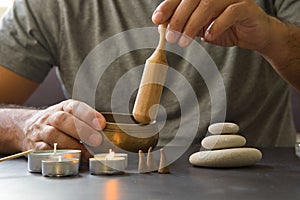 Male hand holding a Tibetan singing bowl to meditate in a relaxed atmosphere with candles and hot stones