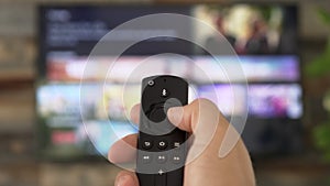 Male hand holding the TV remote control and changing TV channels