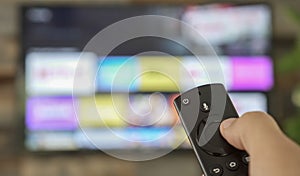 Male hand holding the TV remote control and changing TV channels