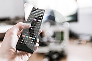 Male hand is holding TV remote control, smart TV