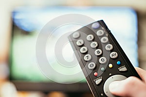 Male hand is holding TV remote control, streaming on a smart TV