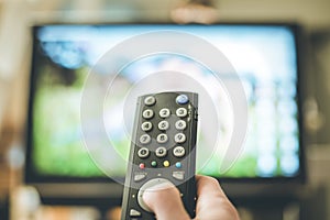 Male hand is holding TV remote control, streaming on a smart TV