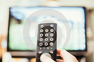 Male hand is holding TV remote control, streaming on a smart TV