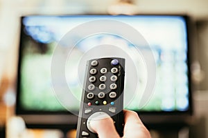 Male hand is holding TV remote control, streaming on a smart TV