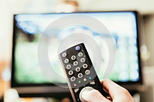 Male hand is holding TV remote control, streaming on a smart TV