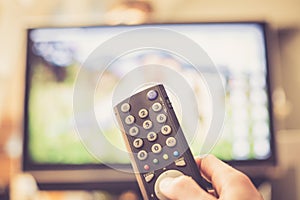 Male hand is holding TV remote control, streaming on a smart TV