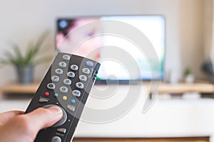 Male hand is holding TV remote control, streaming on a smart TV