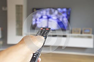 male hand holding tv remote control and watching tv in living room