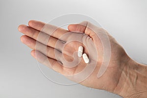 Male hand holding two pills in hand on grey background.