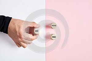 Male hand holding a wooden cube with the word cost pointing at the options of increase or reduce. Business cost management