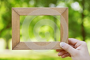 Male hand holding wooden frame against a blurred natural background. Empty space for text. Connecting with nature concept.