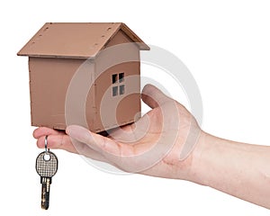 Male hand holding a wooden house model and keys isolated on white background with copy space. Real estate agent concept