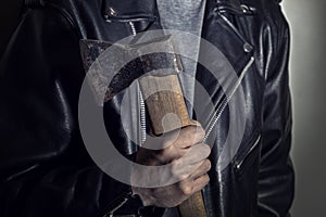 Male hand holds an ax on the background of a leather jacket.