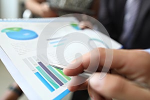Male hand holds ballpoint pen over document with graphs and charts in office closeup
