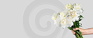 Male hand holds beautiful bouquet of white peonies. Flower delivery concept. Banner format