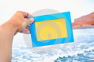 A male hand holds a blue photo frame with empty space seascape on background. Travel concept.