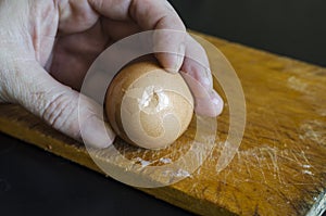 A male hand holds a boiled chicken egg in his shell against the chopping board