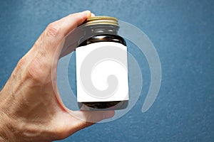 A male hand holds a brown medical glass bottle with a white label for your text and a metal cap