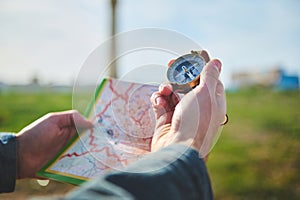 Male hand holds compass with magnetic arrow showing north direction, over a map while discovers a new travel destination