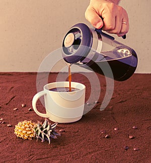 Male hand holds french press and pours coffee into a cup