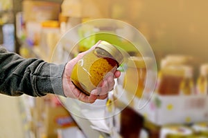 Male hand holds honey on blurred background, row of shelves with groceries in supermarket, concept of marketing, prices for