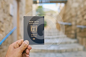 Male hand holds an Israel passport on the old narrow street background