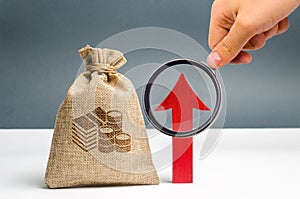 Male hand holds magnifying glass over money bag and up arrow. Concept analysis of profits and budget in the company. Successful