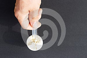 Male hand holds measuring spoon with protein on black background top view.