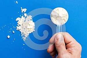 Male hand holds a measuring spoon with protein on blue background top view