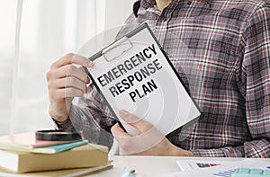 male hand holds a piece of paper with text ERP EMERGENCY RESPONSE PROCEDURES on the background of graphs