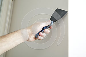 Male hand holds putty knife on the wall near the corner.