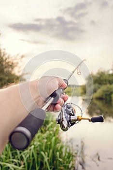 Male hand holds spinning rod on the background of the river