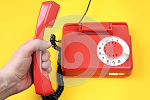A male hand holds a telephone receiver in the hand of a vintage red landline telephone on a yellow background.Classic red telephon