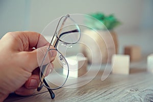 A male hand holds thin-rimmed glasses