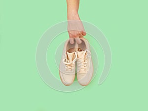 Male hand holds unbranded beige sneakers isolated on green background with copy space. Top view