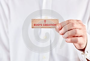 Male hand holds a wooden block with the message God`s Creation. Religion and Christianity
