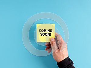 Male hand holds a yellow sticky note paper with the message coming soon