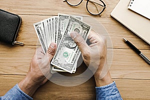 Male hand holing money dollar bill on wood table.