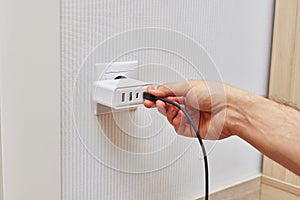 male hand insert a plug of the phone charger into socket.