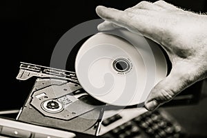 Male hand inserting a DVD into a disk drive. Black and white