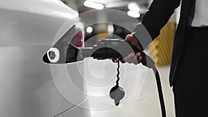 Male hand inserting plug in e-car's port in parking space