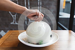 Male hand lifts to up glass cloche from a plate with hot food at restaurant - Smoked food time! Close Up