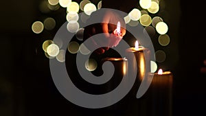 Male hand lights the candles. Close up of three burning candles with blurred Christmas light background