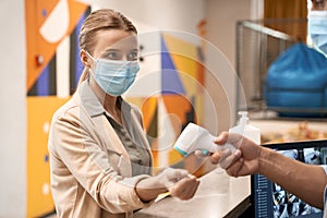 Male hand measuring body temperature of a young businesswoman wearing medical mask or female office worker, temperature
