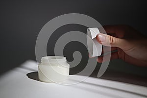 Male hand opens White plastic tube with round cap on white background with shadows. Front view for your design. facial cosmetic pr
