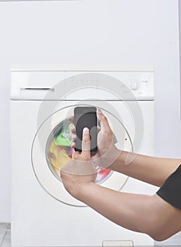 Male hand operate washing machine with his mobile phone