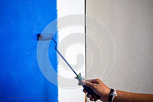 Male hand painting wall in blue with paint roller