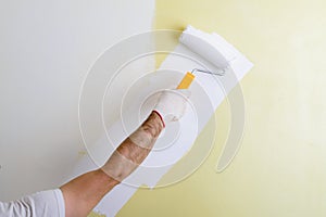 Male hand painting wall with paint roller. Painting new apartment renovating with yellow color paint