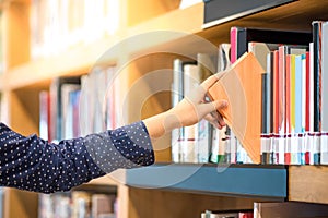 Male hand picking orange book in library