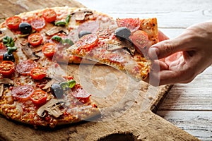 Male hand picking tasty pizza slice.